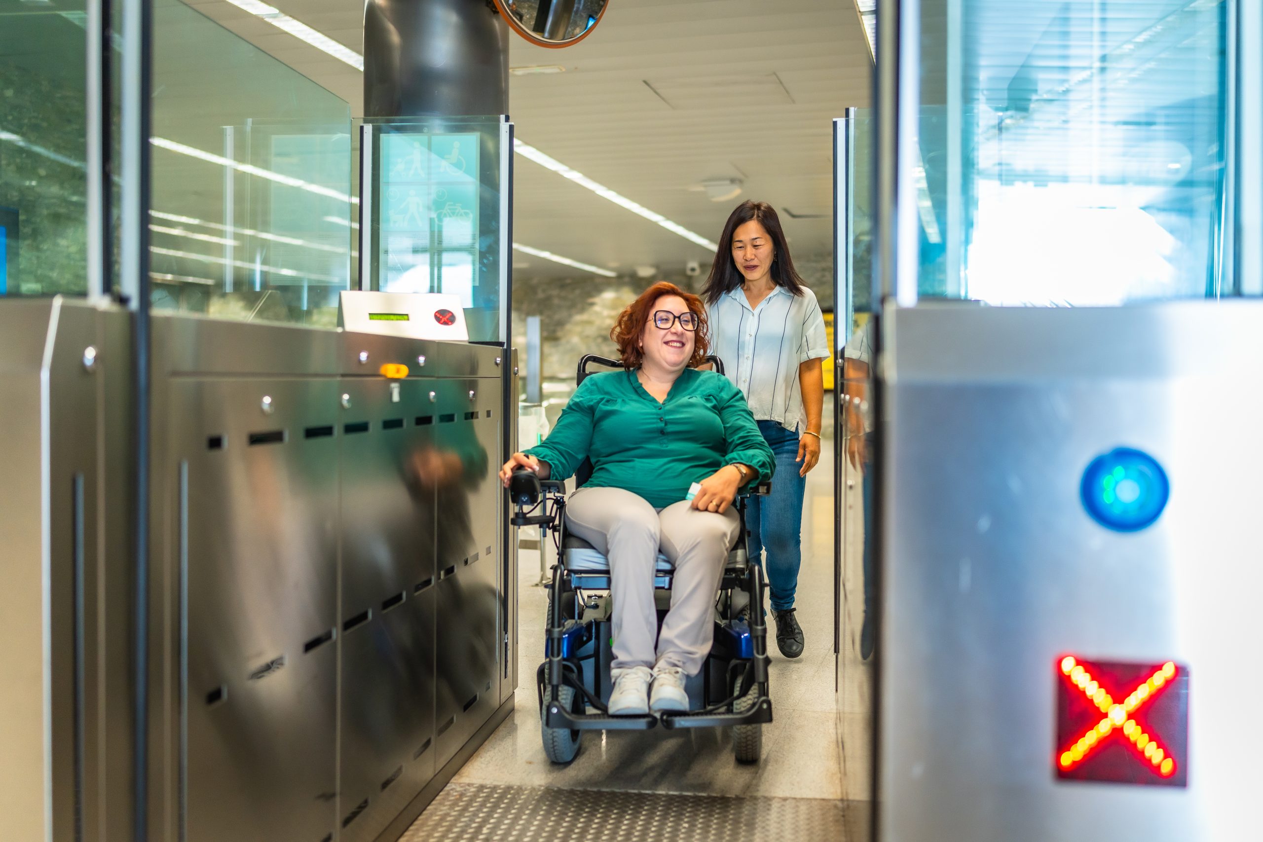 Smiling caucasian adult disabled woman in a wheelchair and chinese caregiver exiting the metro doors