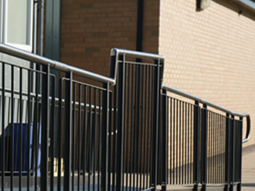 A modular ramp handrail with a raised part ion them, showing 1100mm high balustrade rails. The rails are black with silver connectors.