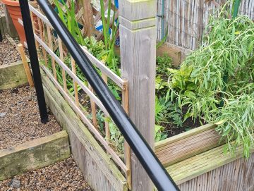 Black powder-coated handrail installed beside garden steps, designed to remain comfortable and not cold to touch in outdoor conditions.