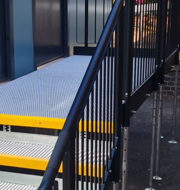 Powder-coated black handrails on an outdoor ramp and steps, designed to provide a comfortable, not cold to touch surface for safer everyday use.