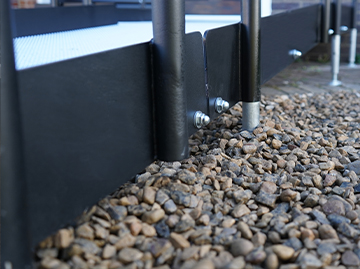 A close up of a black kerb on a ramp. You can see where the legs of the ramp go to the ground, as well as some silver bolts that hold the platform in place.