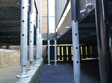 A close up of some legs that help to hold the ramp in place. There are at least 8 legs in view and are all silver with small holes in them where bolts would go.