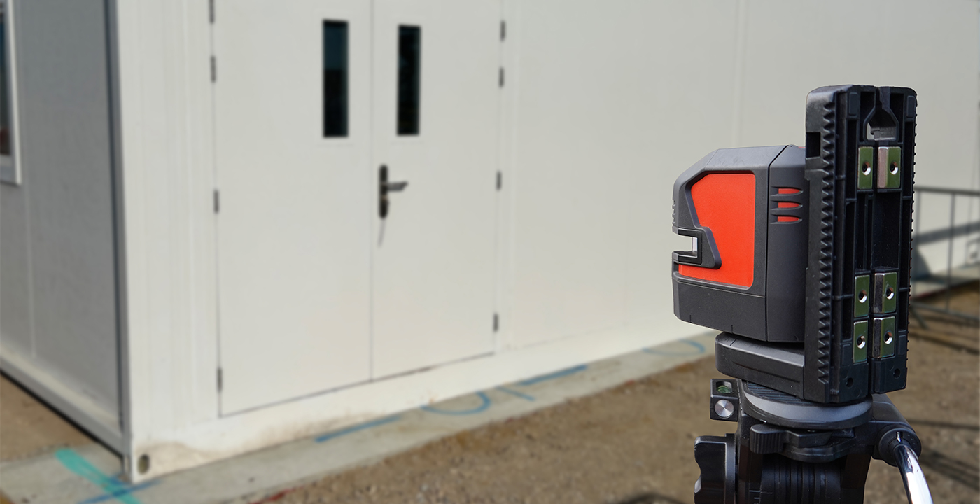 Laser measuring device set up on a tripod outside double doors to assess levels during an access site survey.